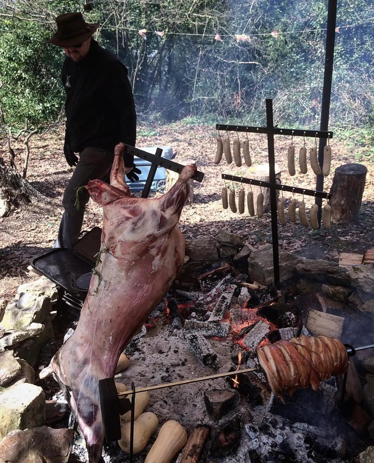 Michael Basco spit-roasting a whole lamb over an open fire, with sausages and squash cooking in the embers
